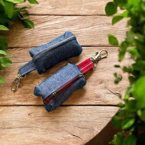 Może przedstawiać: Dwa małe woreczki z dżinsu z czerwonymi i czarnymi kratkami. Jeden woreczek ma srebrny brelok. Oba woreczki leżą na drewnianej powierzchni.
