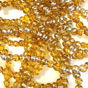 May include: A strand of amber glass beads with silver accents. The beads are round and have a shiny finish.