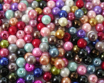 May include: A large assortment of pearl beads in various colors, including pink, purple, green, blue, and white. The beads are all round and have a smooth, glossy finish.