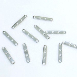 May include: A group of silver metal connector pieces with four holes each. The pieces are rectangular in shape and are scattered on a white surface.