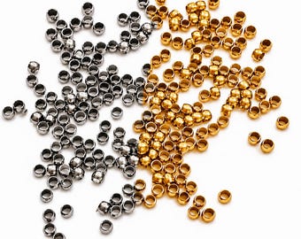 May include: A collection of small, round, metallic crimp beads scattered across the frame. The beads are divided into two distinct color groups: one set features a polished silver finish, while the other set displays a bright, reflective gold tone.
