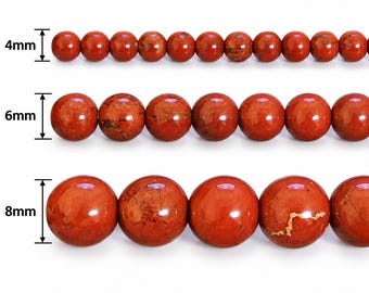 Op de afbeelding: Drie horizontale rijen van ronde, gepolijste rode jaspis kralen. De bovenste rij bevat kralen van 4 mm, de middelste rij kralen van 6 mm en de onderste rij kralen van 8 mm. Elke kraal vertoont natuurlijke donkerbruine en zwarte aders.