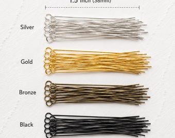 May include: A collection of eye pins arranged in four horizontal rows by color: silver, gold, bronze, and black. Each pin features a circular loop at one end and measures 1.5 inches in length as indicated by the text label above the rows.