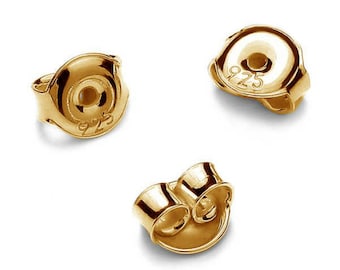 May include: Three gold-colored earring backs. Two of the backs are round with a small hole in the center and the text "925" engraved on the side. The third back is a butterfly shape with two prongs.
