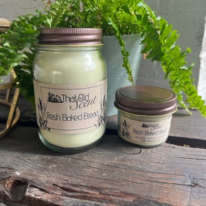 May include: Two glass jars with brown lids and labels that say "That Old Scent" and "Fresh Baked Bread". The jars contain candles.