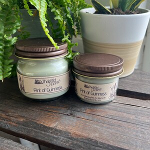 May include: Two glass jars with brown lids containing soy wax candles. The candles are labeled "The Old Scent" and "Pint of Guinness".