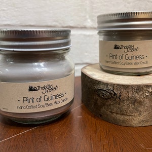 May include: Two glass jars with silver lids containing soy and beeswax candles. The labels on the jars read "That Old Scent" and "Pint of Guiness. Hand Crafted Soy/Bees Wax Candle."