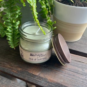 May include: A green glass jar candle with a brown lid. The candle is labeled "That Old Scent" and "Pint of Guinness".