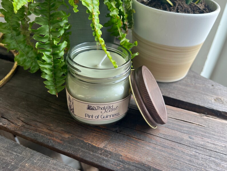 May include: A green glass jar candle with a brown lid. The candle is labeled "That Old Scent" and "Pint of Guinness".