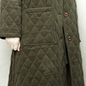 May include: A long, quilted jacket in a dark green color. The jacket has a button closure and a patch pocket on the left side.