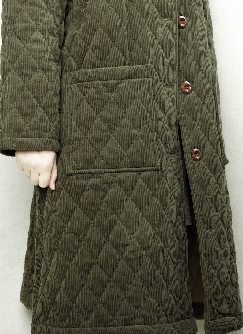 May include: A long, quilted jacket in a dark green color. The jacket has a button closure and a patch pocket on the left side.
