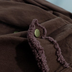 Op de afbeelding: Een bruin denim jack met een gefranst randdetail en een metalen knoop.