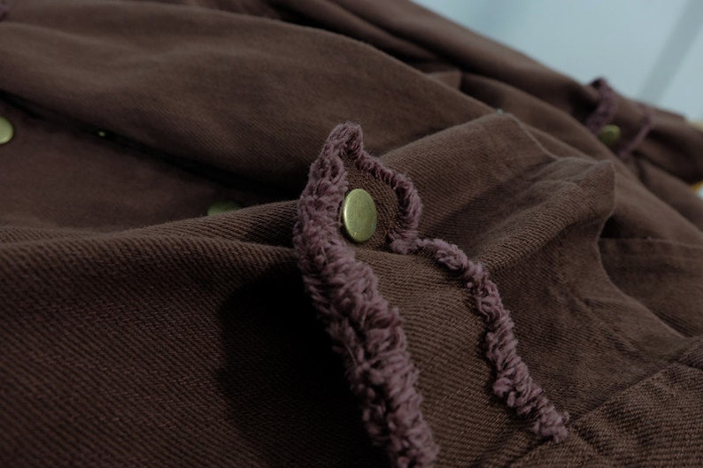 Op de afbeelding: Een bruin denim jack met een gefranst randdetail en een metalen knoop.