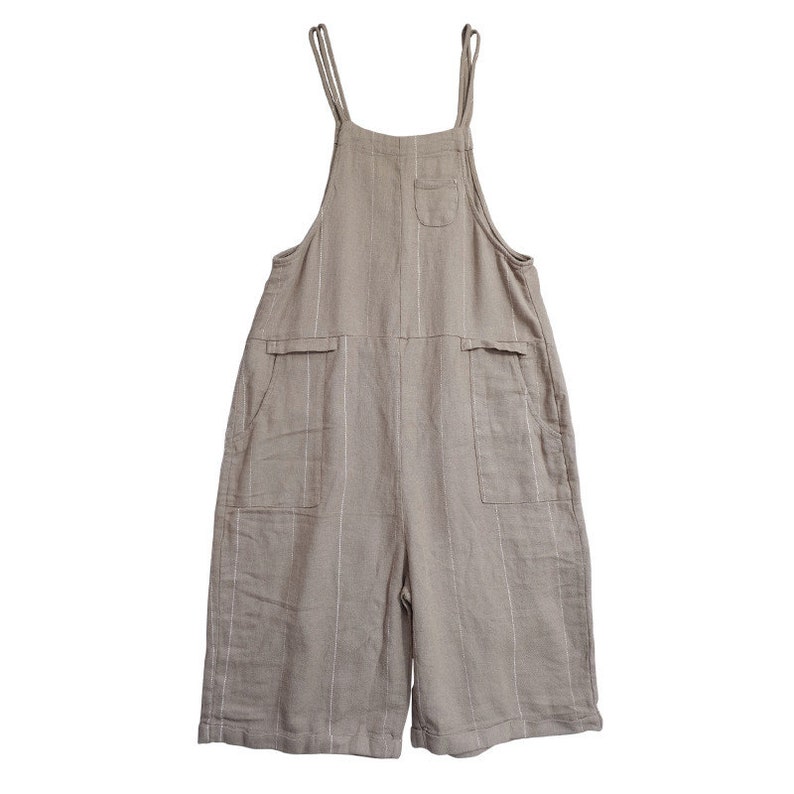 May include: A pair of beige linen overalls with thin white stripes. The overalls have two large pockets on the front and a smaller pocket on the chest.