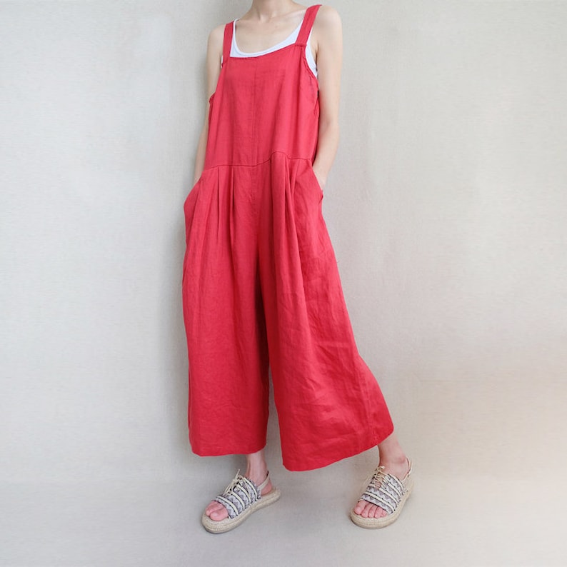 May include: A red linen jumpsuit with wide legs and thin shoulder straps. The jumpsuit has pockets on the sides and a relaxed fit.