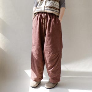 May include: A pair of loose-fitting, wide-leg pants in a deep burgundy color. The pants have a drawstring waistband and are made of a soft, textured fabric.