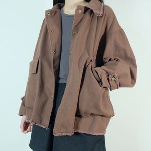 Op de afbeelding: Een oversized bruin jack met een rafelige zoom en een knoopsluiting. Het jack heeft grote zakken aan de voorkant en een ontspannen pasvorm.