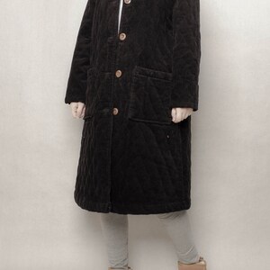 May include: A long black quilted corduroy coat with a button closure and two patch pockets. The coat is lined with a soft, warm material and has a relaxed fit.