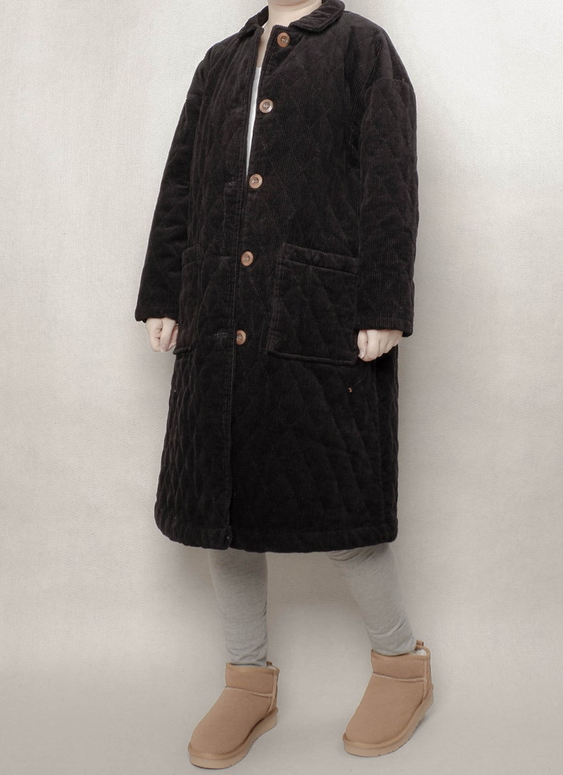 May include: A long black quilted corduroy coat with a button closure and two patch pockets. The coat is lined with a soft, warm material and has a relaxed fit.