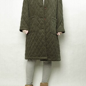 May include: A long, quilted, green corduroy coat with a button closure and two patch pockets. The coat is worn over grey leggings and brown ankle boots.