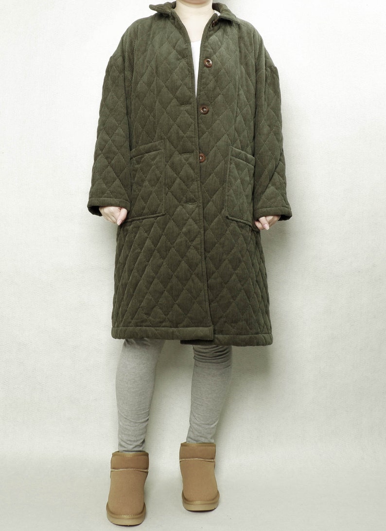 May include: A long, quilted, green corduroy coat with a button closure and two patch pockets. The coat is worn over grey leggings and brown ankle boots.