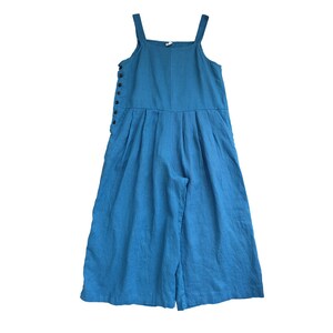 May include: A blue linen overall jumpsuit with a button closure on the side. The straps are adjustable and the legs are wide-legged.