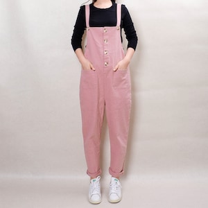 May include: A dusty rose colored overall with a button front and two front pockets. The overall has thin straps and is made of a soft, casual fabric.