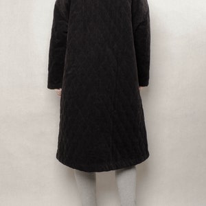 May include: A long black quilted corduroy coat with a stand-up collar. The coat is worn over grey leggings and brown suede ankle boots.