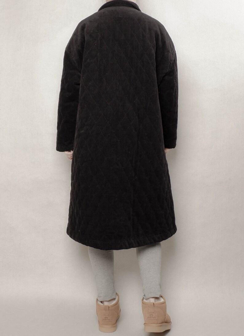 May include: A long black quilted corduroy coat with a stand-up collar. The coat is worn over grey leggings and brown suede ankle boots.