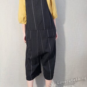 May include: Black and white striped linen overalls with thin straps. The overalls have a relaxed fit and are cropped above the ankle. The model is wearing brown shoes.