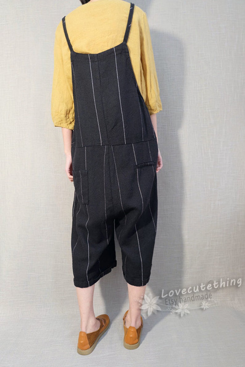 May include: Black and white striped linen overalls with thin straps. The overalls have a relaxed fit and are cropped above the ankle. The model is wearing brown shoes.