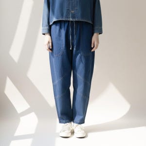 May include: A denim outfit featuring a cropped jacket and high-waisted, loose-fitting pants with a drawstring waist. The pants have large front pockets and are paired with white sneakers. The outfit is a medium blue wash.