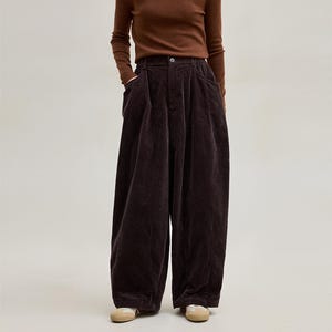 May include: A person wearing a brown long-sleeved top and dark brown corduroy trousers. The trousers have a wide leg design and pockets. The person is also wearing beige shoes.