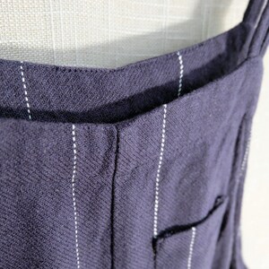 May include: A close-up of a dark blue pinstripe overall with thin white stripes. The straps are visible at the top of the image.