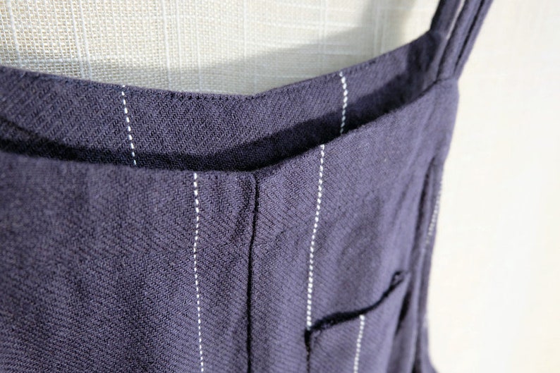 May include: A close-up of a dark blue pinstripe overall with thin white stripes. The straps are visible at the top of the image.