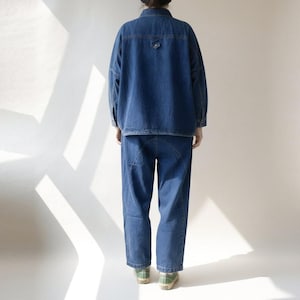 May include: A denim jacket and matching pants set in a medium blue wash. The jacket has a button closure and a small pocket detail. The pants are loose-fitting with a unique seam design. The outfit is casual and comfortable.