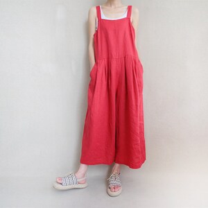 May include: A red linen jumpsuit with wide legs and thin straps. The jumpsuit has a relaxed fit and is made of a lightweight fabric.