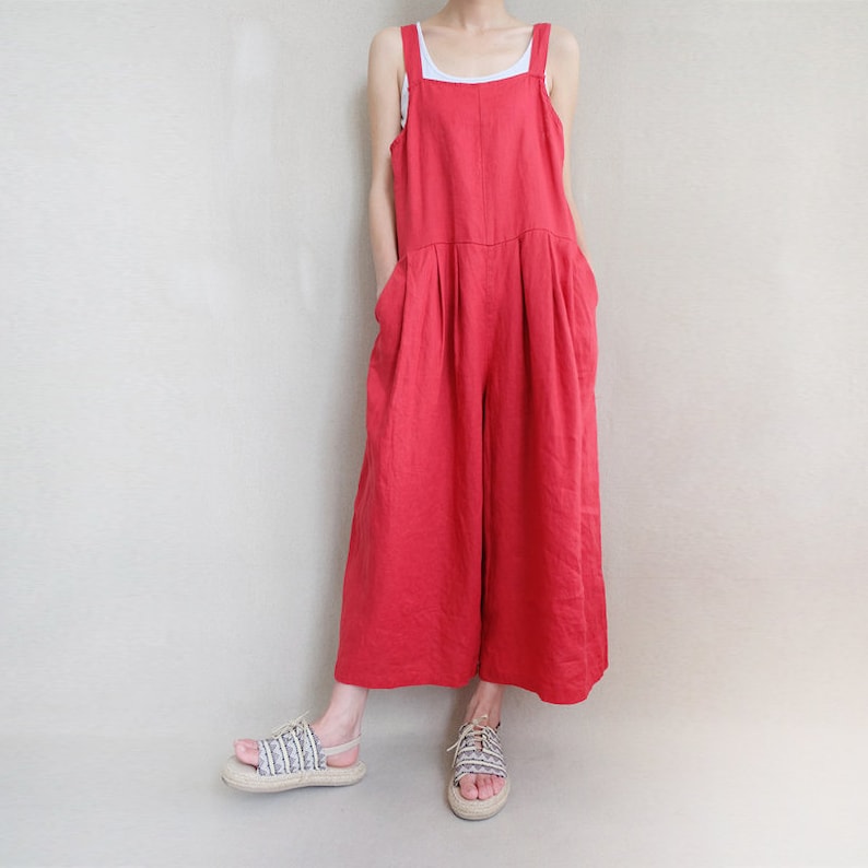 May include: A red linen jumpsuit with wide legs and thin straps. The jumpsuit has a relaxed fit and is made of a lightweight fabric.