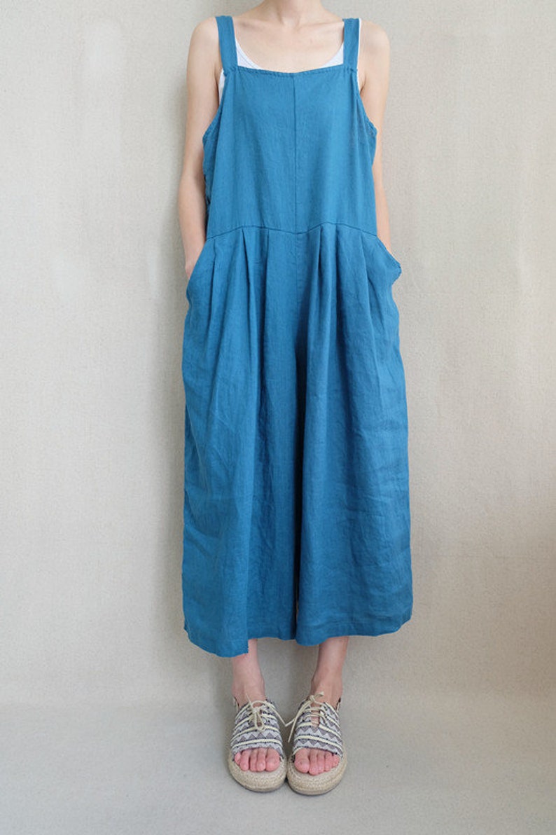 May include: A teal blue linen overall jumpsuit with wide legs and a square neckline. The straps are adjustable and the pockets are large.