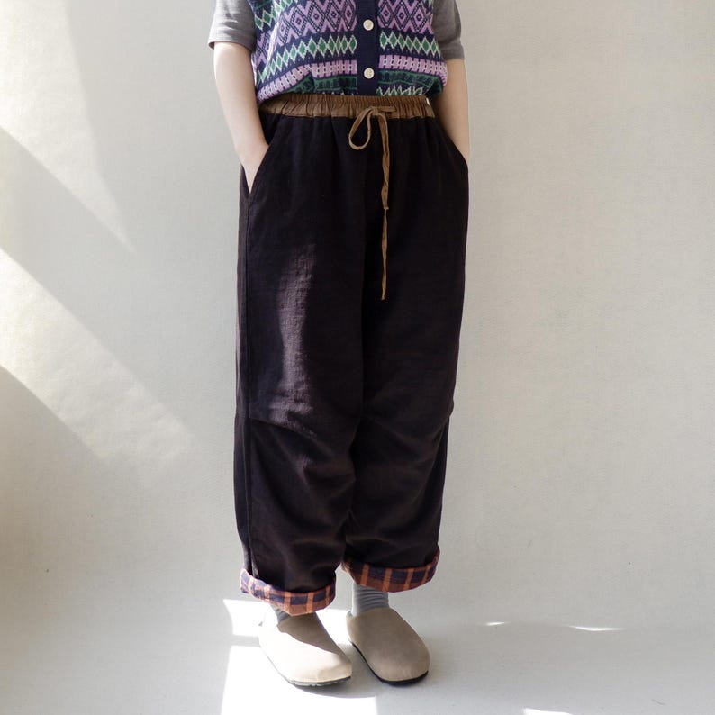 May include: Black wide-leg pants with a brown elastic waistband and drawstring. The pants have a plaid trim at the bottom of the legs.