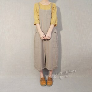 May include: A brown linen overall dress with thin vertical stripes and large pockets. The dress has adjustable straps and a relaxed fit. The model is wearing a yellow top underneath the dress.