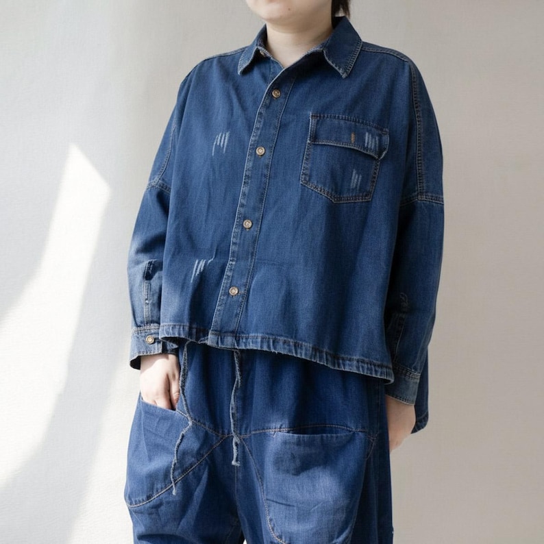 May include: A denim shirt and matching pants set in a medium blue wash. The shirt has a button-down front, a chest pocket, and distressed details. The pants have a relaxed fit with a drawstring waist and large pockets. The outfit is casual and stylish.