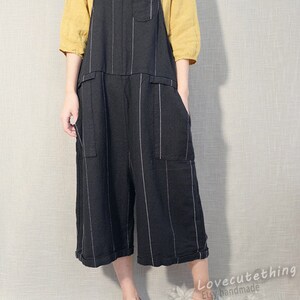 May include: Black and white striped linen overalls with adjustable straps. The overalls have two large pockets on the front and a smaller pocket on the chest. The model is wearing the overalls with a yellow linen top and brown leather shoes.