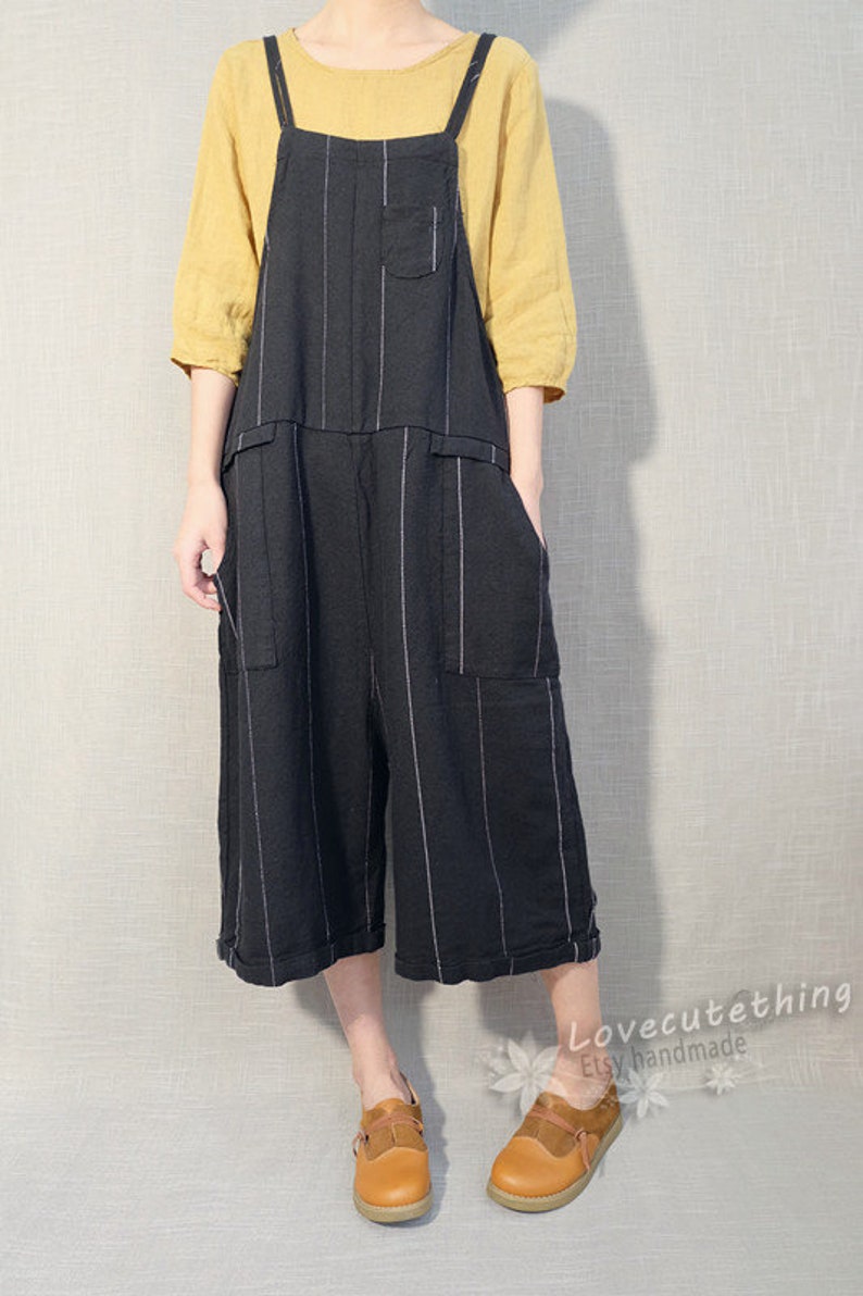 May include: Black and white striped linen overalls with adjustable straps. The overalls have two large pockets on the front and a smaller pocket on the chest. The model is wearing the overalls with a yellow linen top and brown leather shoes.
