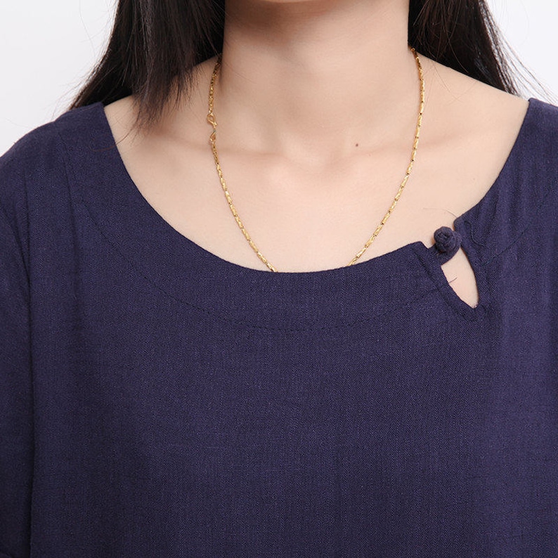 May include: A navy blue top with a round neckline and a single button closure. The top has a small slit at the neckline.