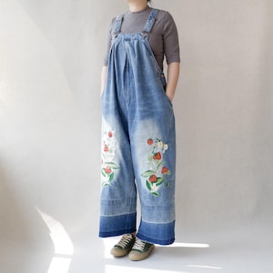 May include: Wide-leg denim dungarees with embroidered floral and strawberry designs. The dungarees are a light blue wash with a faded look.