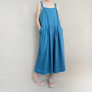 May include: A teal blue linen overall dress with thin straps. The dress has a relaxed fit and a wide leg.
