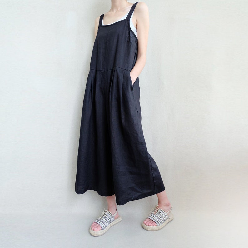 May include: A black linen jumpsuit with wide legs and a square neckline. The jumpsuit has adjustable straps and pockets on the sides.