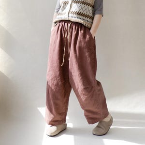 May include: A pair of loose-fitting, wide-leg pants in a deep burgundy color. The pants have a drawstring waist and are made of a soft, textured fabric.
