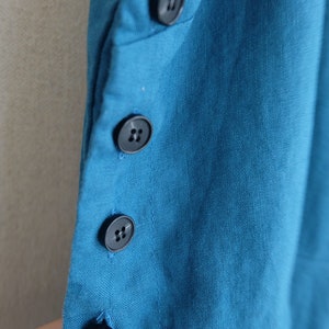 May include: A close-up of a teal blue fabric with four black buttons. The buttons are sewn on the fabric in a vertical line.